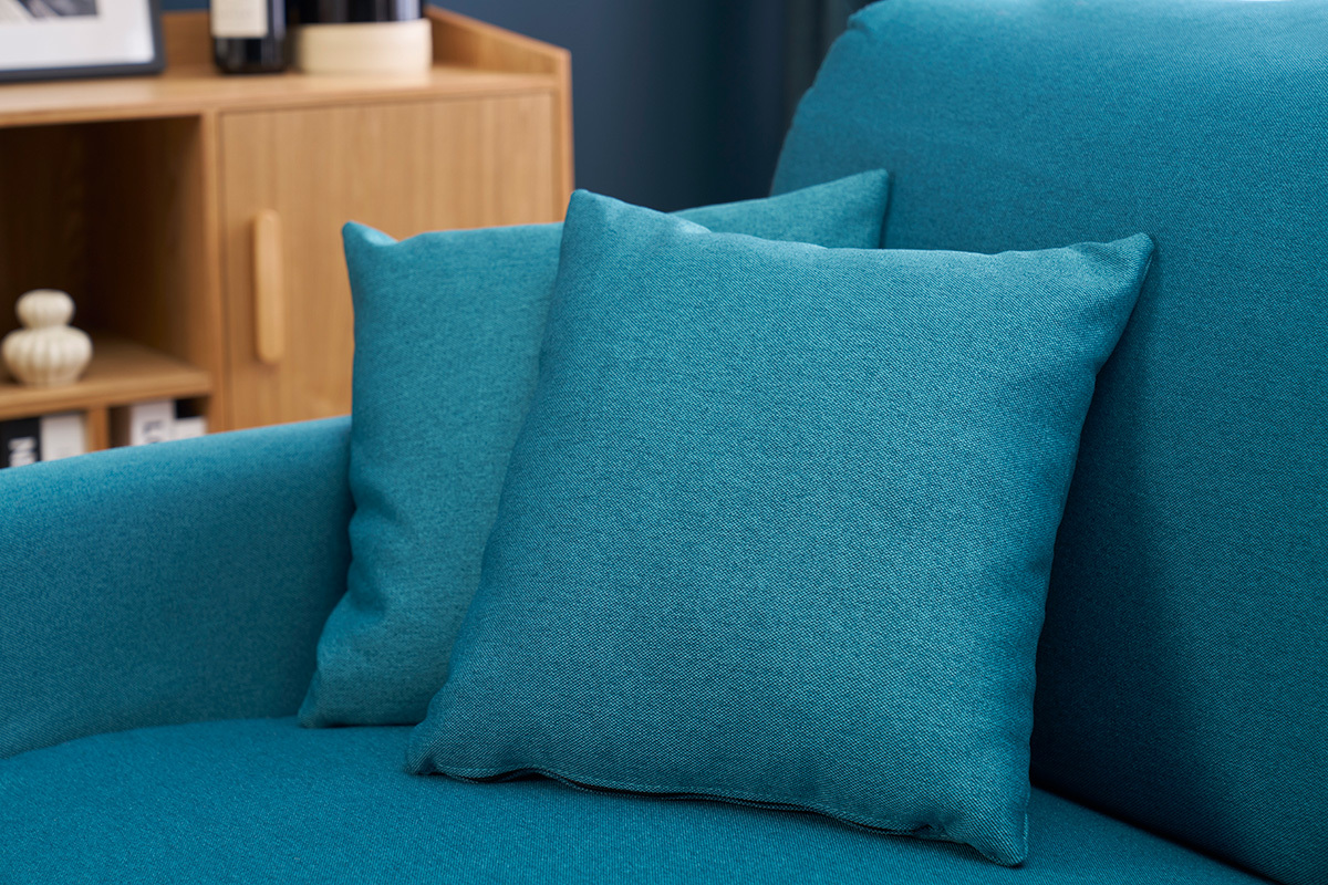 Coussins du canap� convertible bleu canard SKANDY en vue rapproch�e � c�t� d'un meuble en bois.