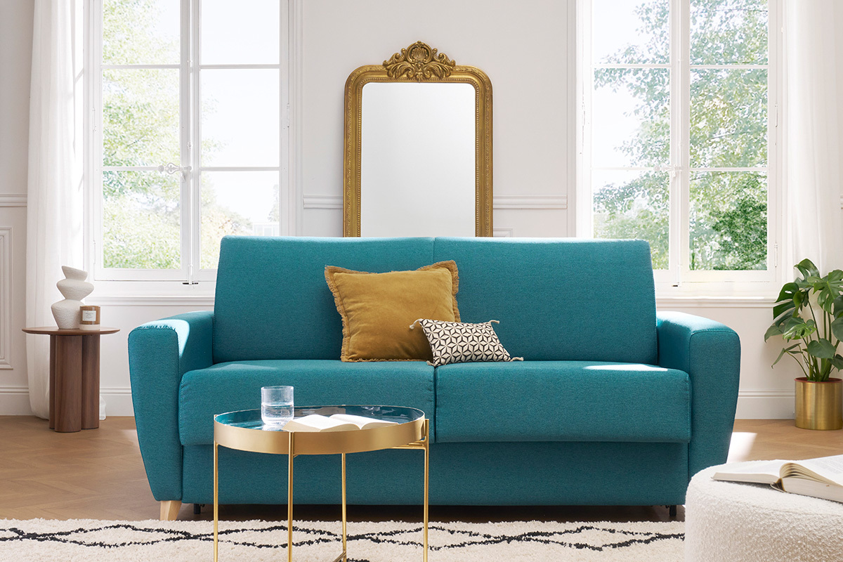 Canap� bleu canard 3 places avec coussins, vue de face, table basse dor�e, miroir en arri�re-plan.