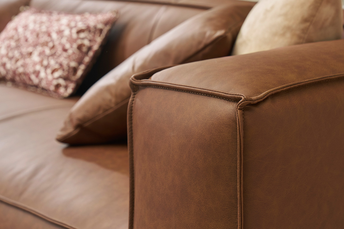 Accoudoir du canap� d'angle en cuir marron avec coussins.