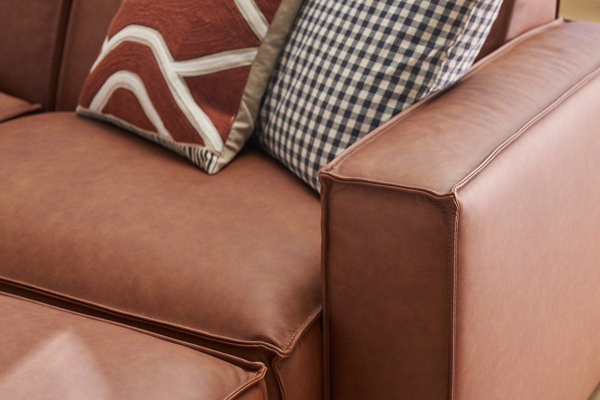 Gros plan sur un canap� en cuir marron avec coussins � motifs.