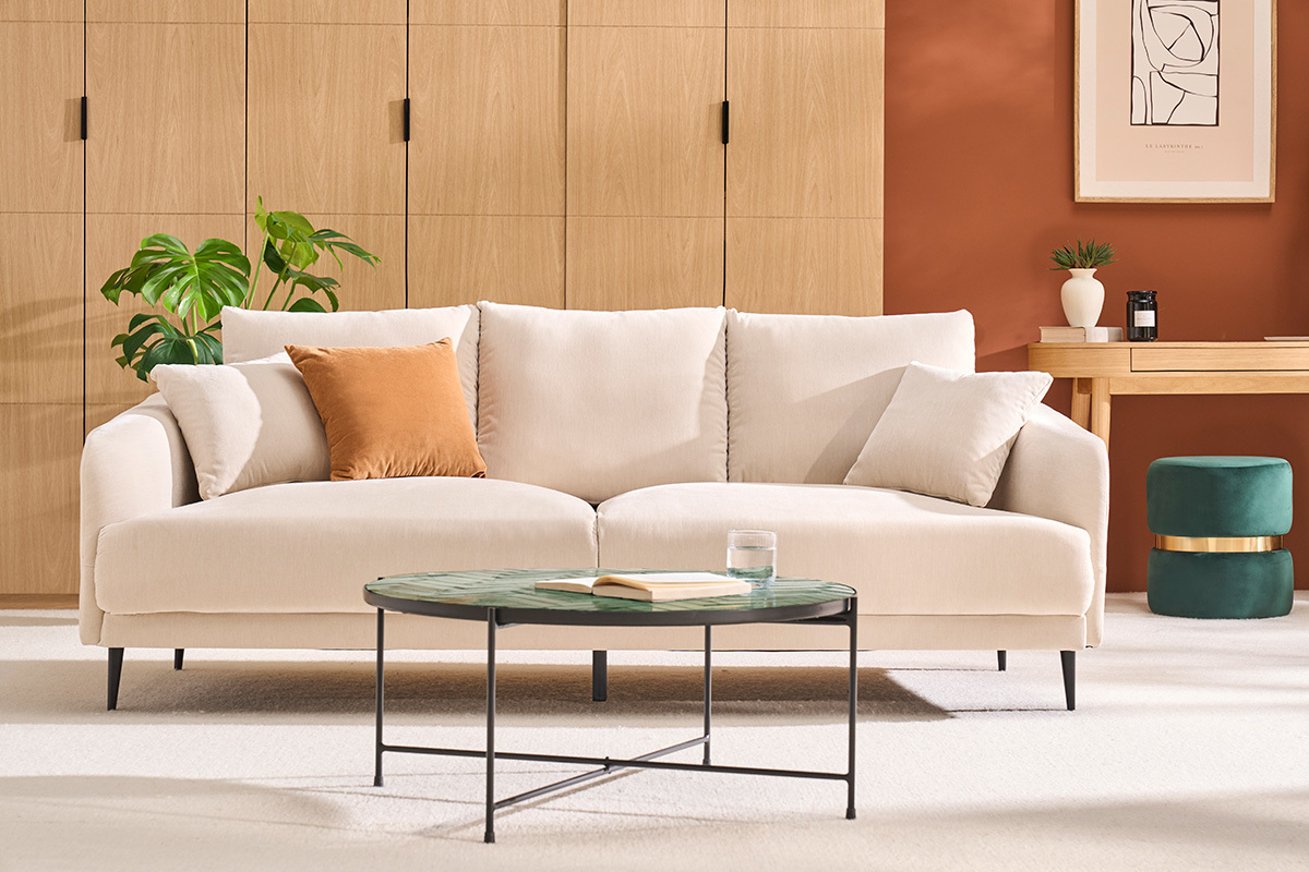 Canap� 3 places beige effet velours, pieds m�tal noir, devant table basse, int�rieur moderne.