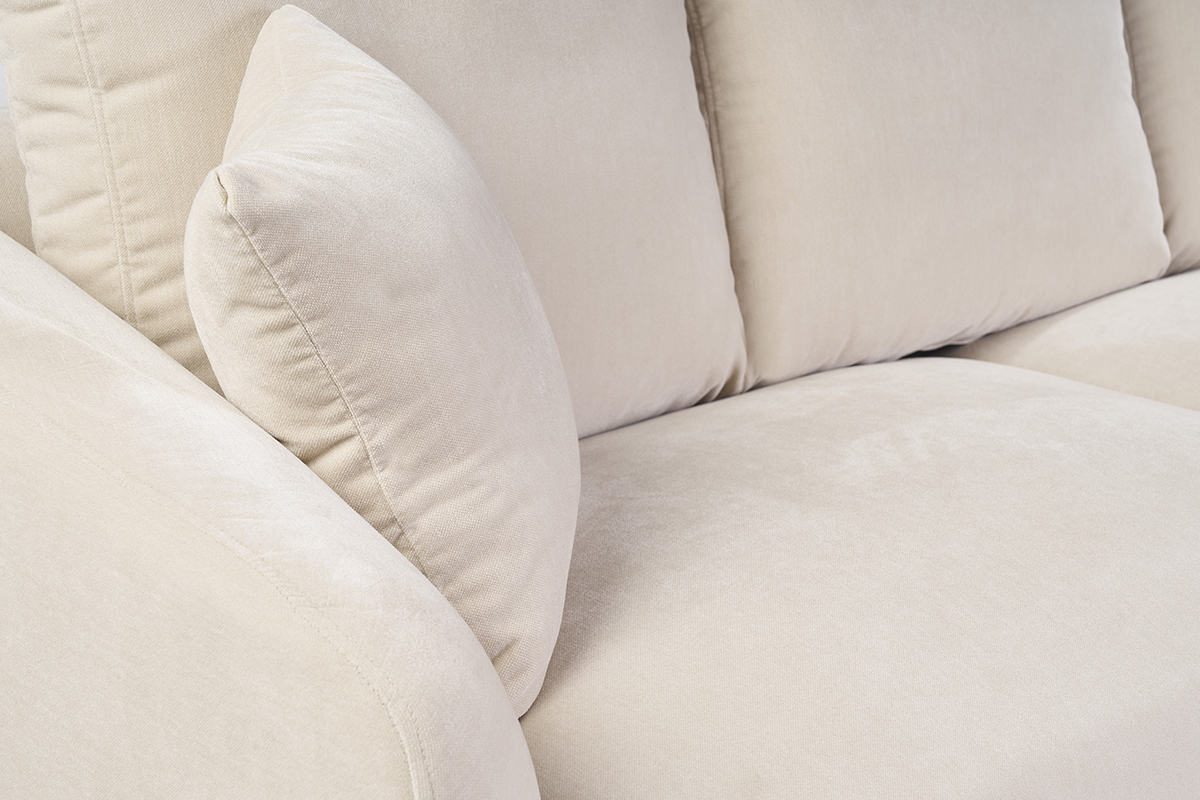 D�tail du canap� beige en tissu effet velours, coussin et accoudoir visibles, vue de pr�s.