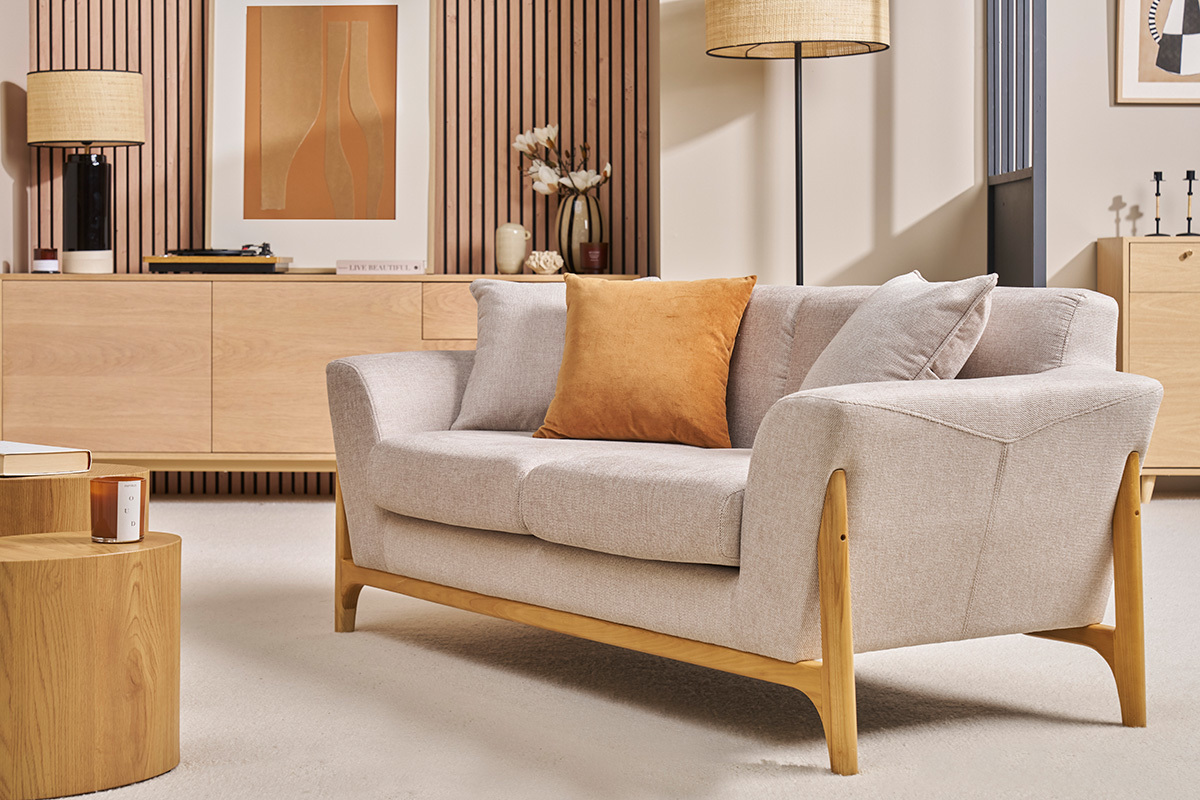 Canap� 2 places beige en tissu et bois clair, vue d'angle, avec coussin orange.