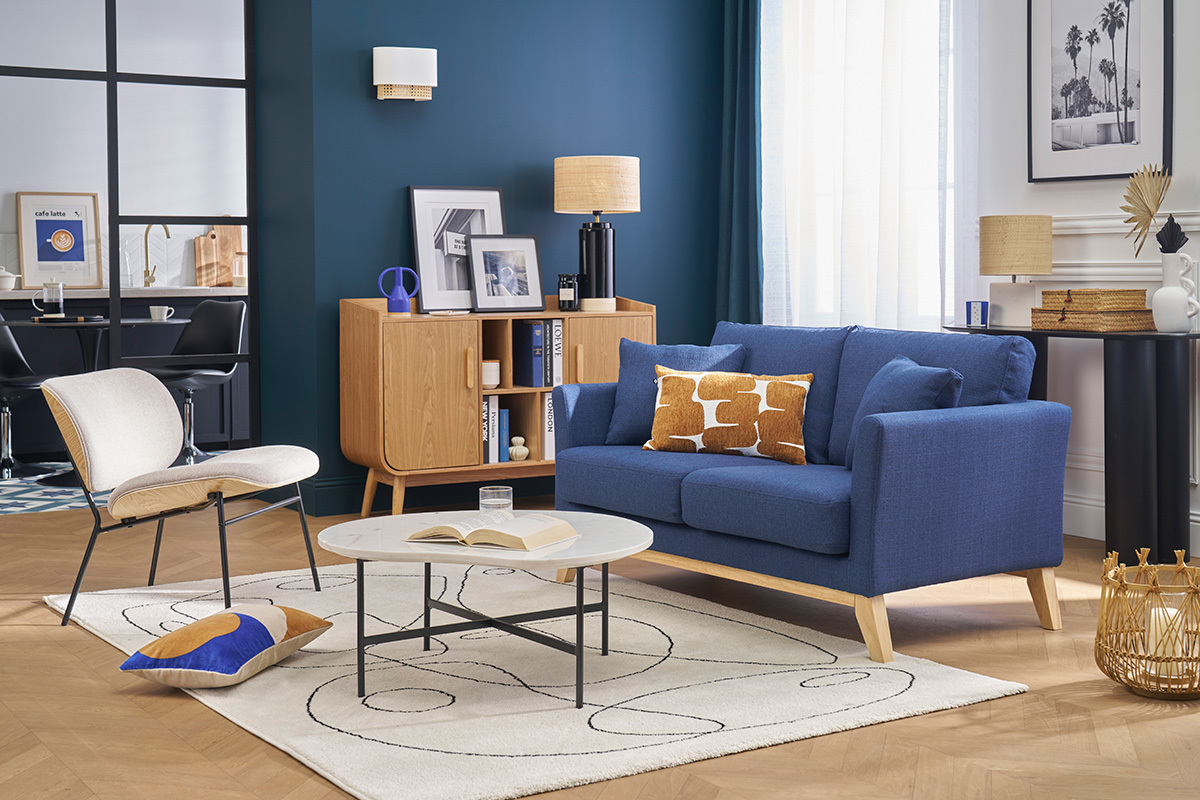 Salon avec canap� scandinave bleu fonc� en tissu et pieds en bois, table basse et meuble en bois clair.
