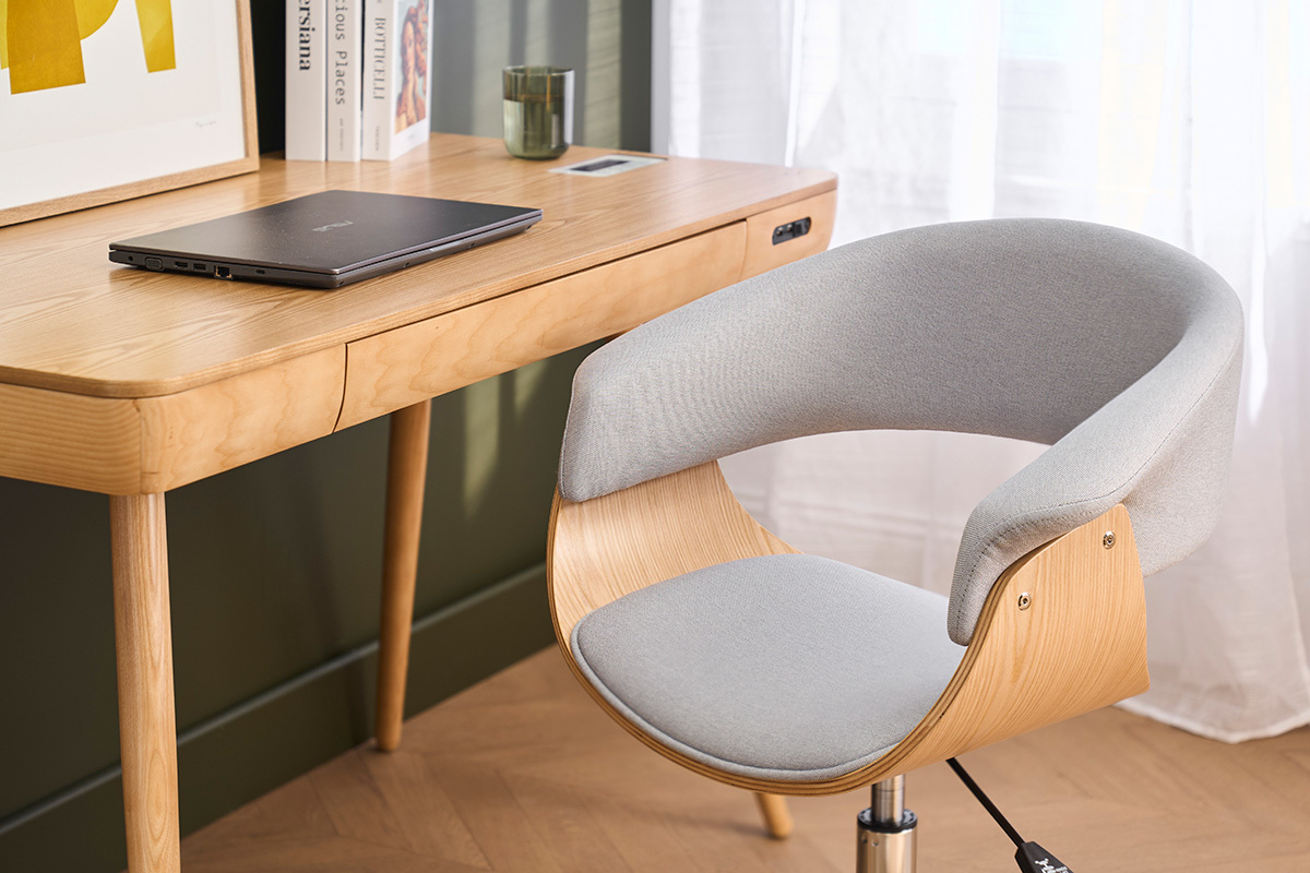 Chaise de bureau grise avec roulettes devant un bureau en bois clair, vue de c�t�.