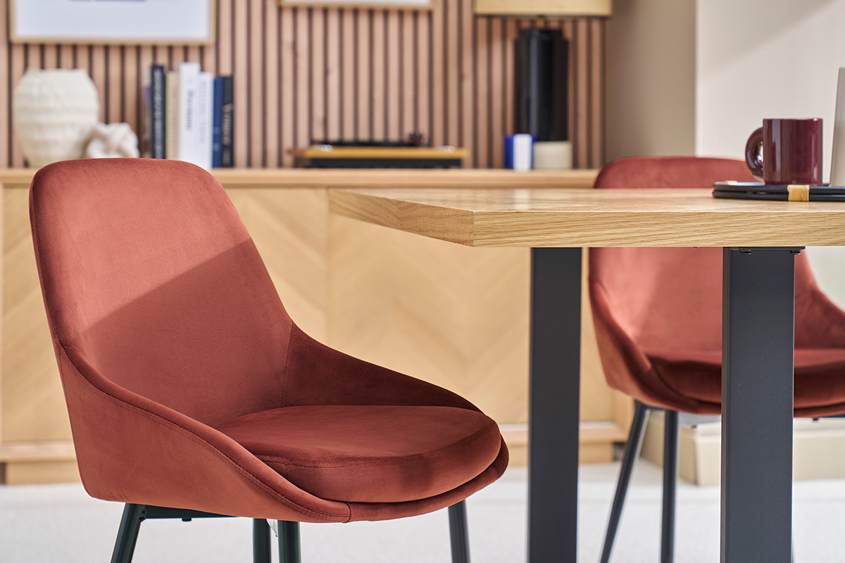 Deux chaises en velours rouge tomette et m�tal noir entourant une table en bois.