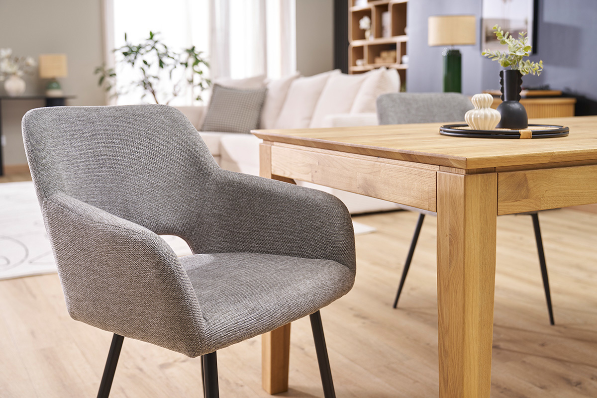 Chaise en tissu effet velours gris avec pieds en m�tal noir, vue 3/4 pr�s d'une table en bois.