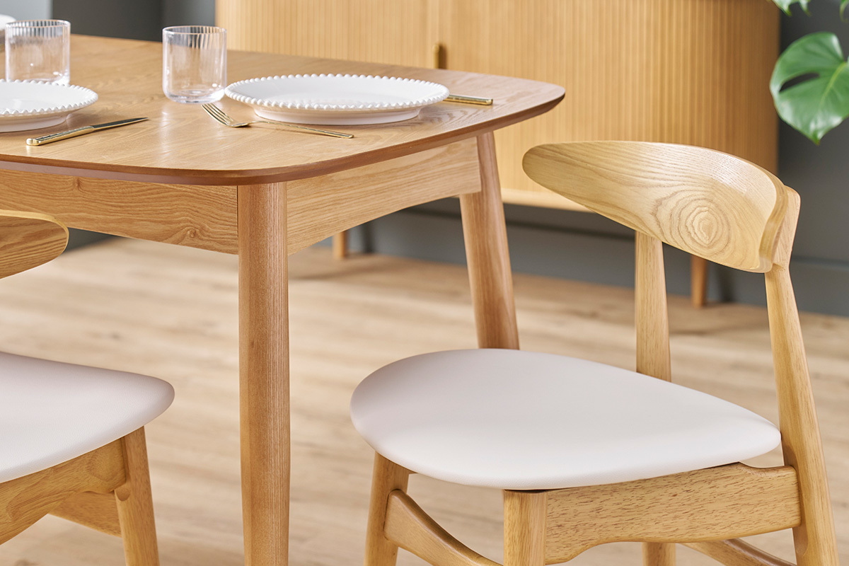 Chaises scandinaves en bois clair avec assise blanche autour d'une table, vue d'angle.