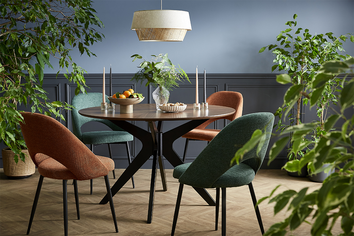 Salle � manger avec chaises vertes et orange en tissu effet velours, autour d'une table ronde en bois.