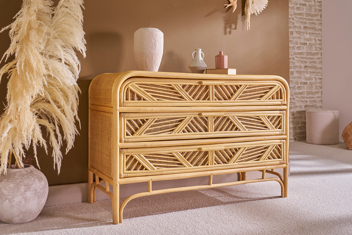 Commode en rotin � 3 tiroirs avec d�tails de cannage, vue de profil, entour�e de d�corations.