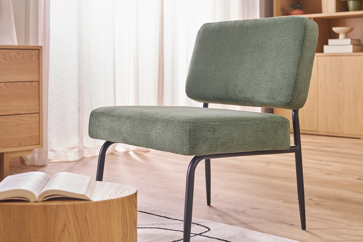 Fauteuil en tissu vert kaki et m�tal noir, vue de c�t� dans un salon lumineux.