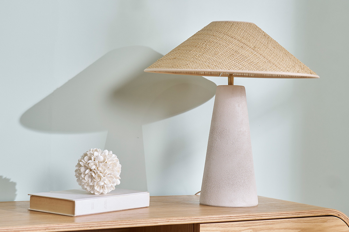 Lampe � poser blanche en c�ramique avec abat-jour en rabane, sur une table en bois.