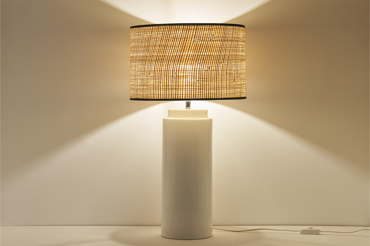 Lampe en c�ramique blanche avec abat-jour en raphia allum�e, vue de face.