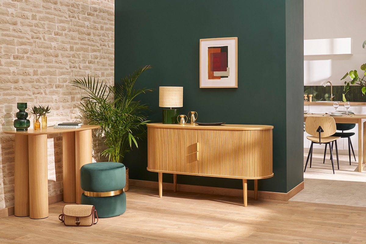 Pouf rond en velours vert, plac� pr�s d'un meuble en bois dans un salon moderne.
