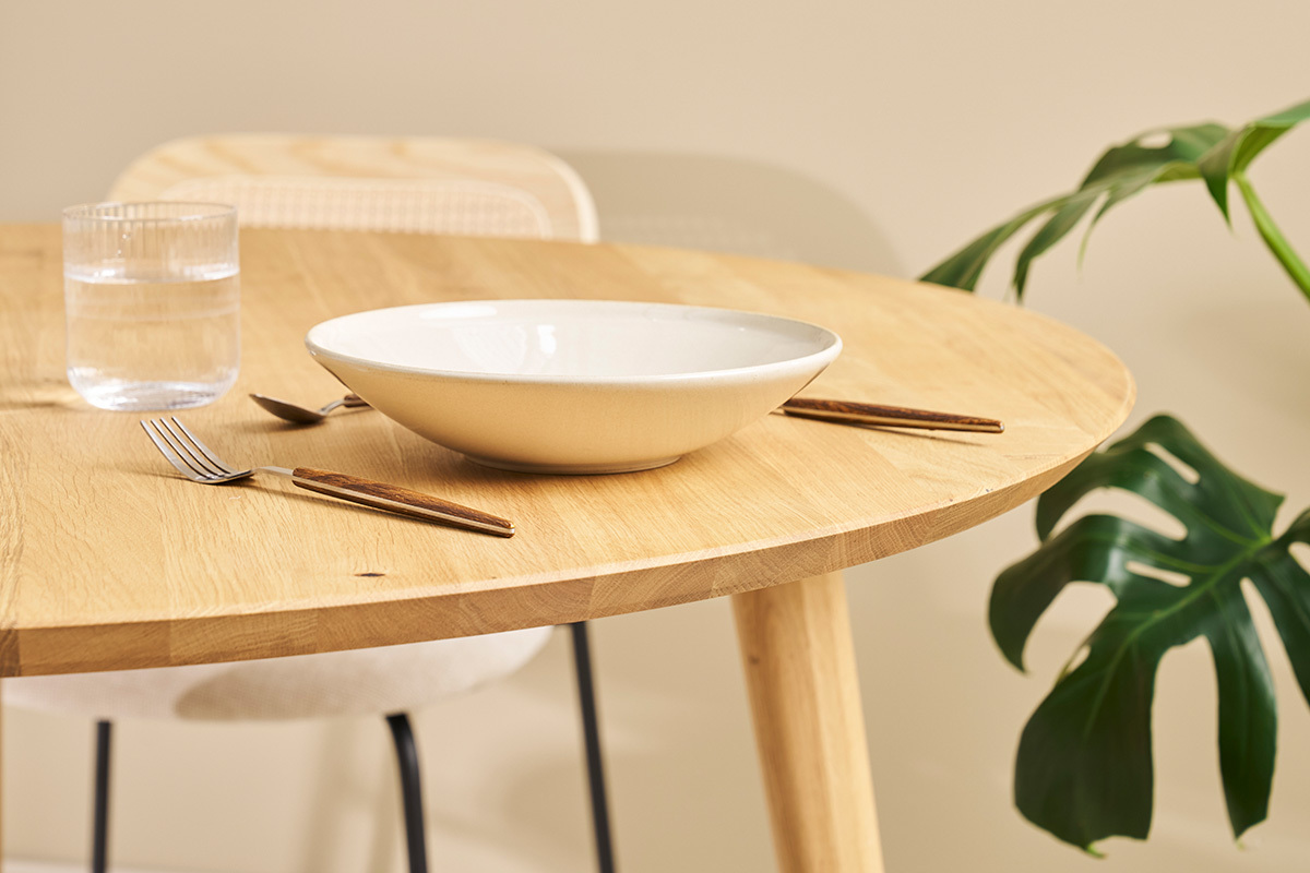 Table ronde en ch�ne clair avec vaisselle et plante en arri�re-plan, vue rapproch�e.