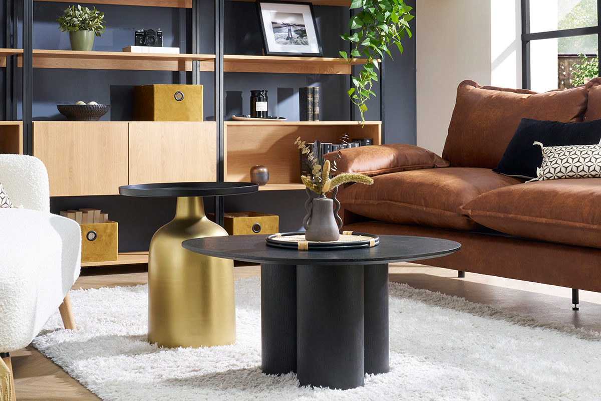 Table basse HOLLEN noire en bois avec trois pieds cylindriques, vue sur tapis clair dans salon.