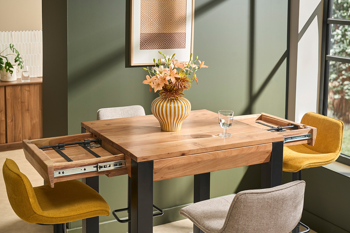 Table de bar extensible en bois massif et m�tal avec rallonges d�ploy�es, fleurs en vase sur le plateau.