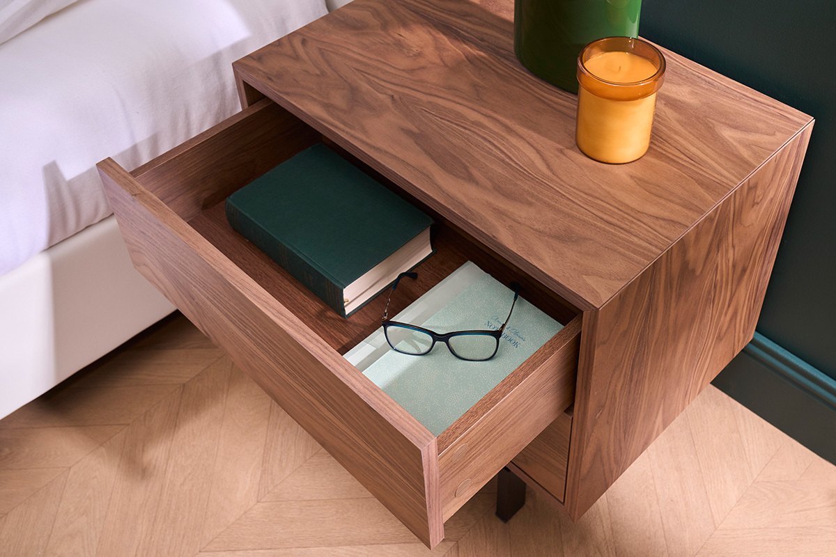 Table de chevet bois fonc� avec tiroir ouvert contenant livre et lunettes.