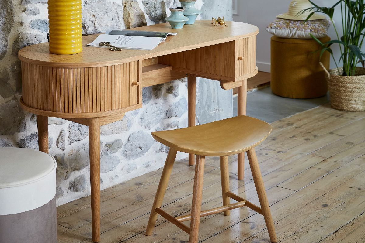 Tabouret bas en bois clair devant un bureau en bois sur sol en parquet.