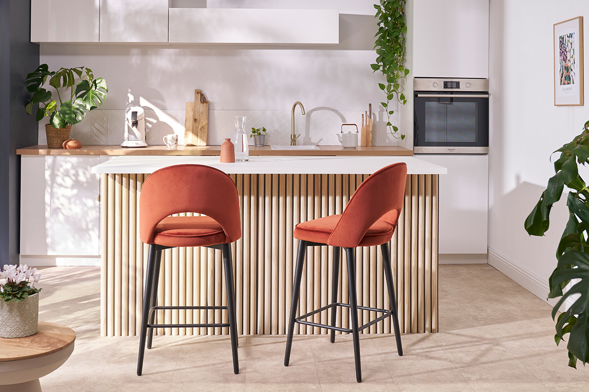 Deux tabourets de bar en velours orange avec pieds en m�tal noir, autour d'un �lot de cuisine.