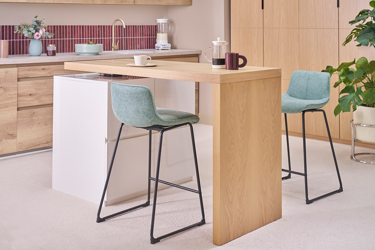 Tabourets de bar en tissu vert c�ladon et m�tal noir autour d'un comptoir en bois clair.