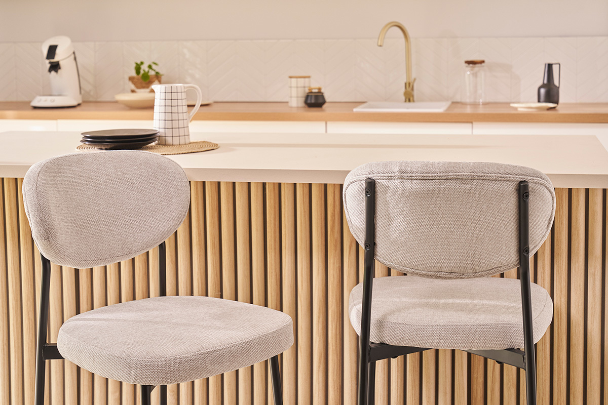 Deux tabourets de bar BREKA en tissu beige vus de dos devant un comptoir.