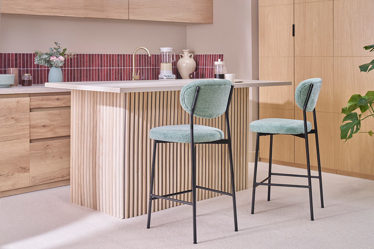 Deux tabourets de bar verts en tissu velours c�ladon et m�tal noir devant un �lot de cuisine.