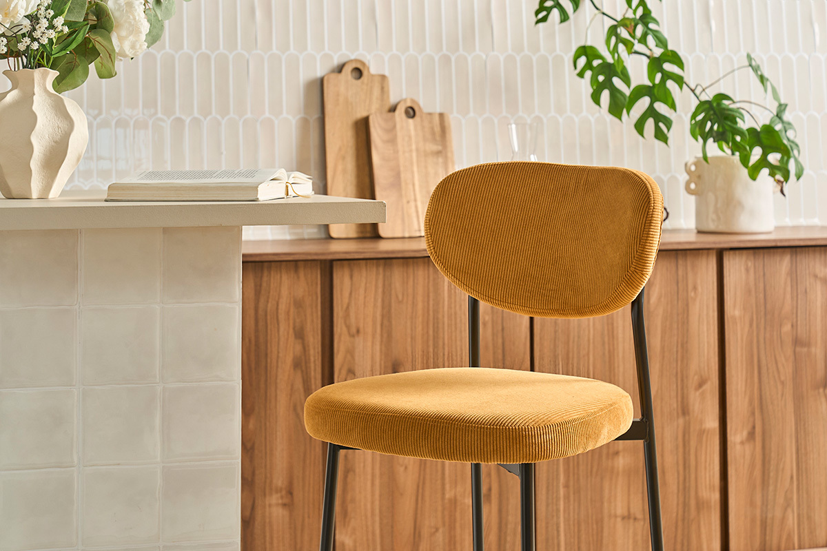 Tabouret de bar fixe en tissu velours c�tel� jaune curry, vue lat�rale, avec d�cor en arri�re-plan.