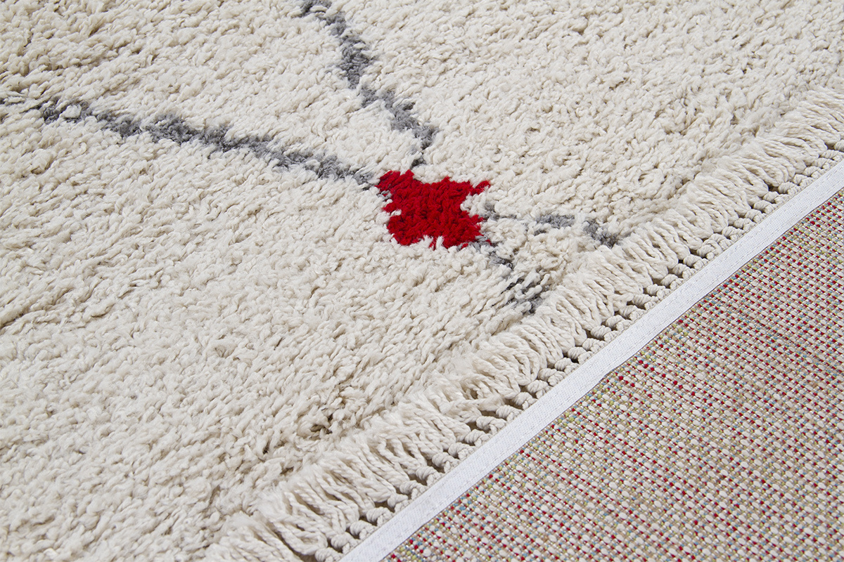 Gros plan sur un tapis LIO beige avec motifs losanges gris et rouge, bordure � franges.